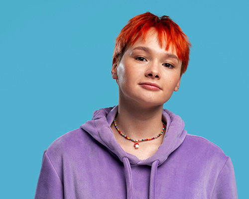 LGBTQIA girl with red hair and purple pullover looking happy