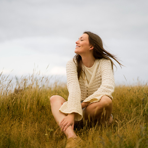 Woman sitting on a field looking happy and peaceful.