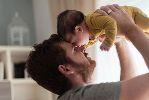 Dad holding baby up, touching heads, and dad smiling and happy.