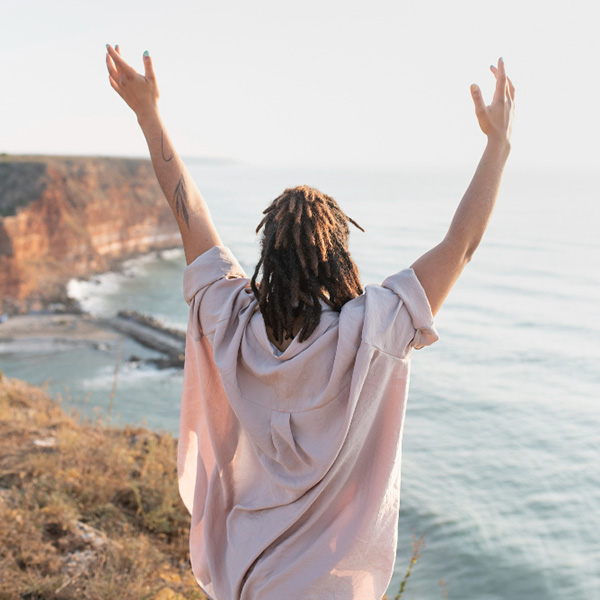 Woman on cliff above beach with hands up exhibiting joy and freedom.