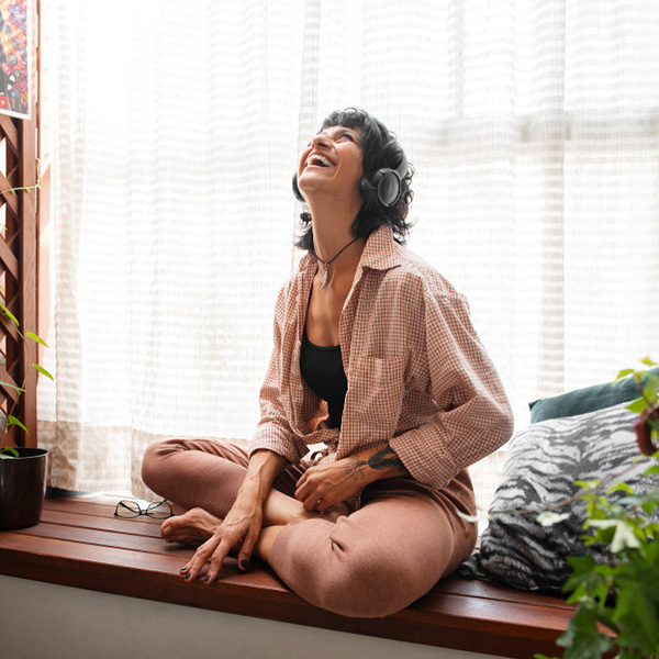 Woman listening to headphones while sitting in a windowseat. She is laughing and happy.