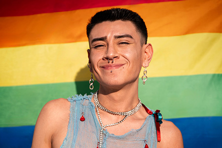 LGBTQIA+ man with face piercings standing confidently in front of LGBTQ flag