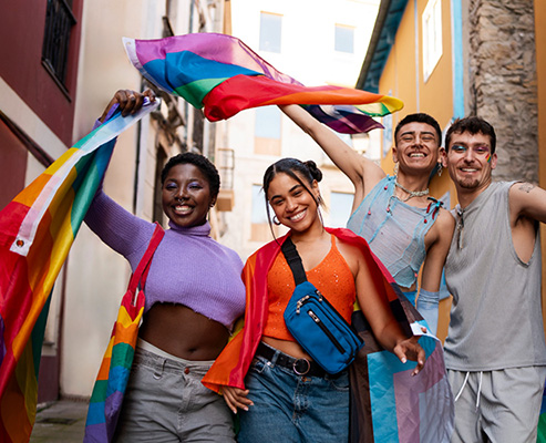 LGBTQIA+ group smiling and waving LGBTQIA+ flags during a pride festival