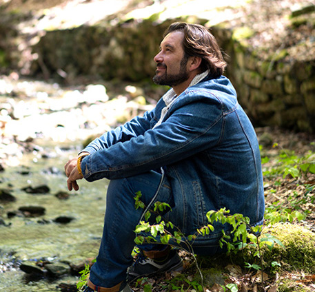 Man sitting on a rock by a stream looking pensive.