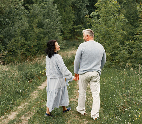 Man and woman hold hands walking down a forest path. They are walking away from the photographer.
