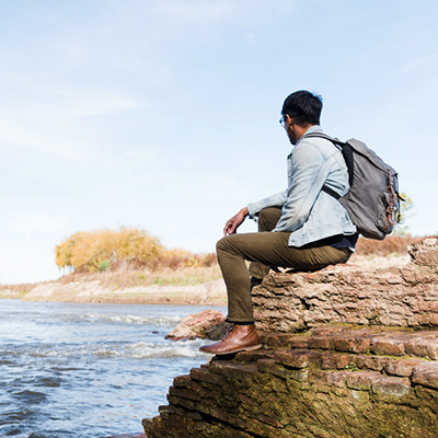 Man sitting on rock by river looking into the distance and feeling calm and peaceful.