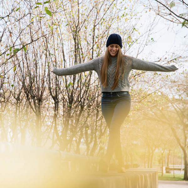 Woman walking along a log with arms outstretched looking happy and carefree.